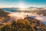 Ein Wanderer steht im herbstlichen Licht auf einer Bergkuppe in den Bergen und schaut auf die Nebelsuppe im Tal.