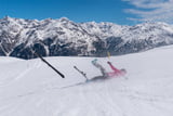 Eine weibliche Skifahrerin hat auf einer Skipiste einen Unfall und stürtzt in Sölden und beide Skier lösen sich sie rutscht ins Tal.