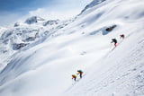 Vier Personen fahren bei sonnigem Wetter einen verschneiten steilen Hang auf Tourenski in einer winterlichen Landschaft im Lechtal ab.