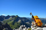 Wanderstöcke an einem gelben Wanderrucksack, im Hintergrund sind Berge zu sehen.