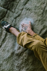 Ein Kletterer hält sich mit Hand und Fuß an einer schmalen Kante fest.