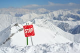 Gefahrschild "Stopp" steckt im Schnee, im Hintergrund sind zahlreiche Berge zu sehen.