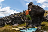 Ein Mann klettert draußen an einem Felsblock ohne Seil, er bouldert also, und trägt eine grüne Hose.